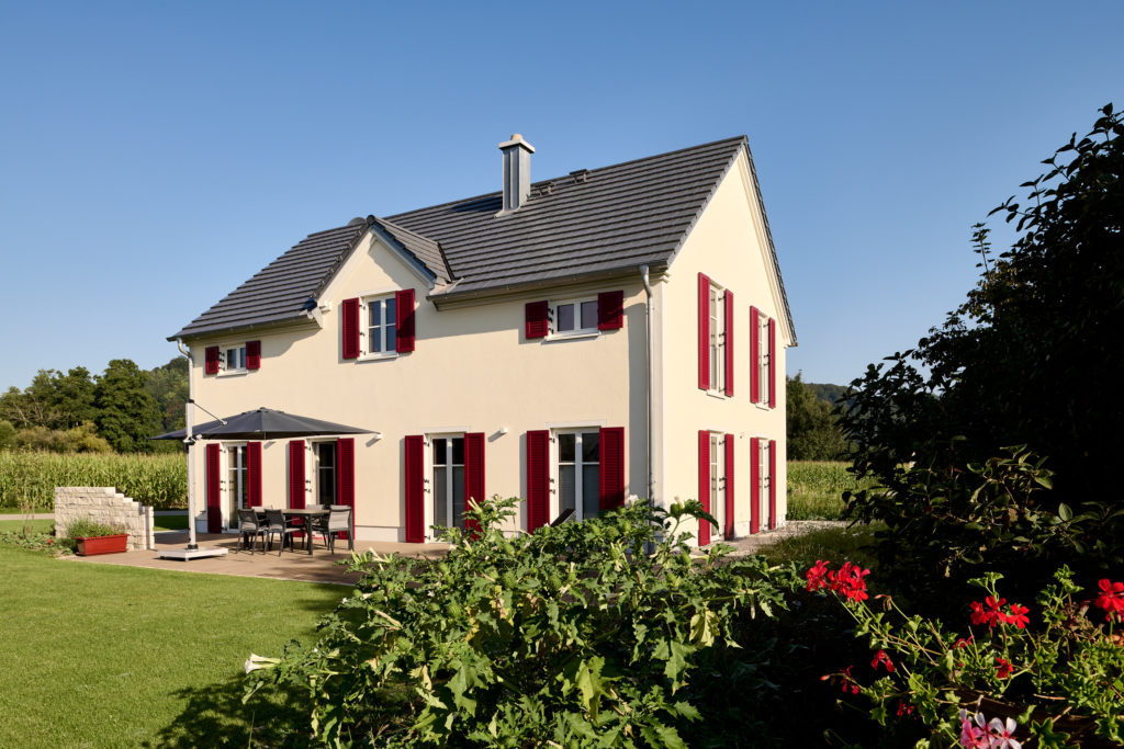 Außenansicht Holzhaus mit steilem Satteldach und roten Fensterläden an Fenstern und Türen