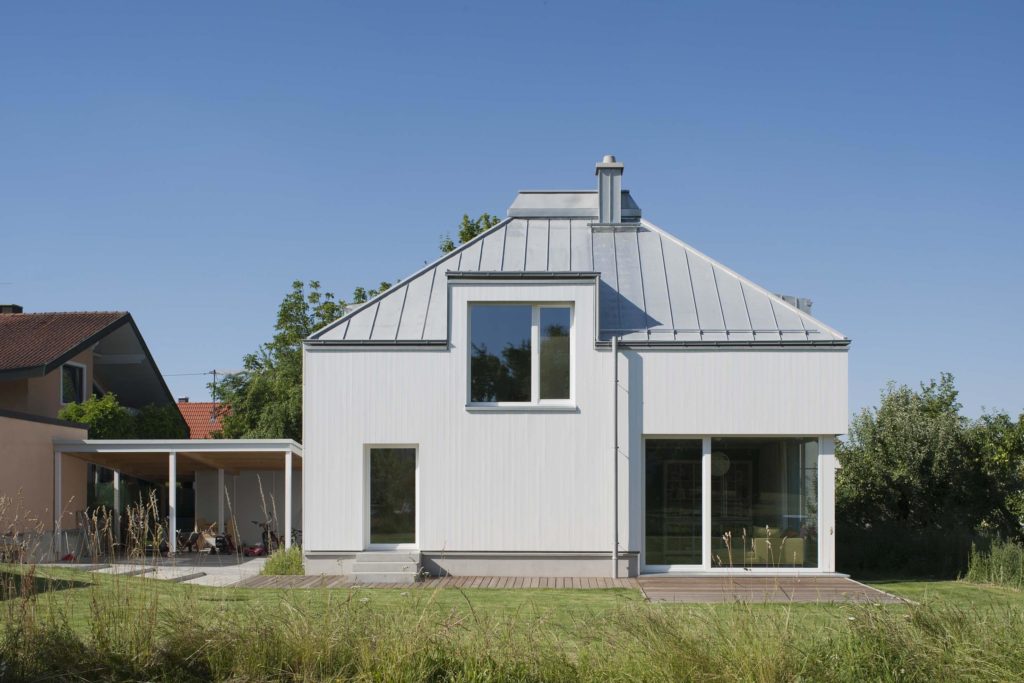 Außenansicht Holzhaus mit weißer Holzfassade und Zeltdach aus Titanzink