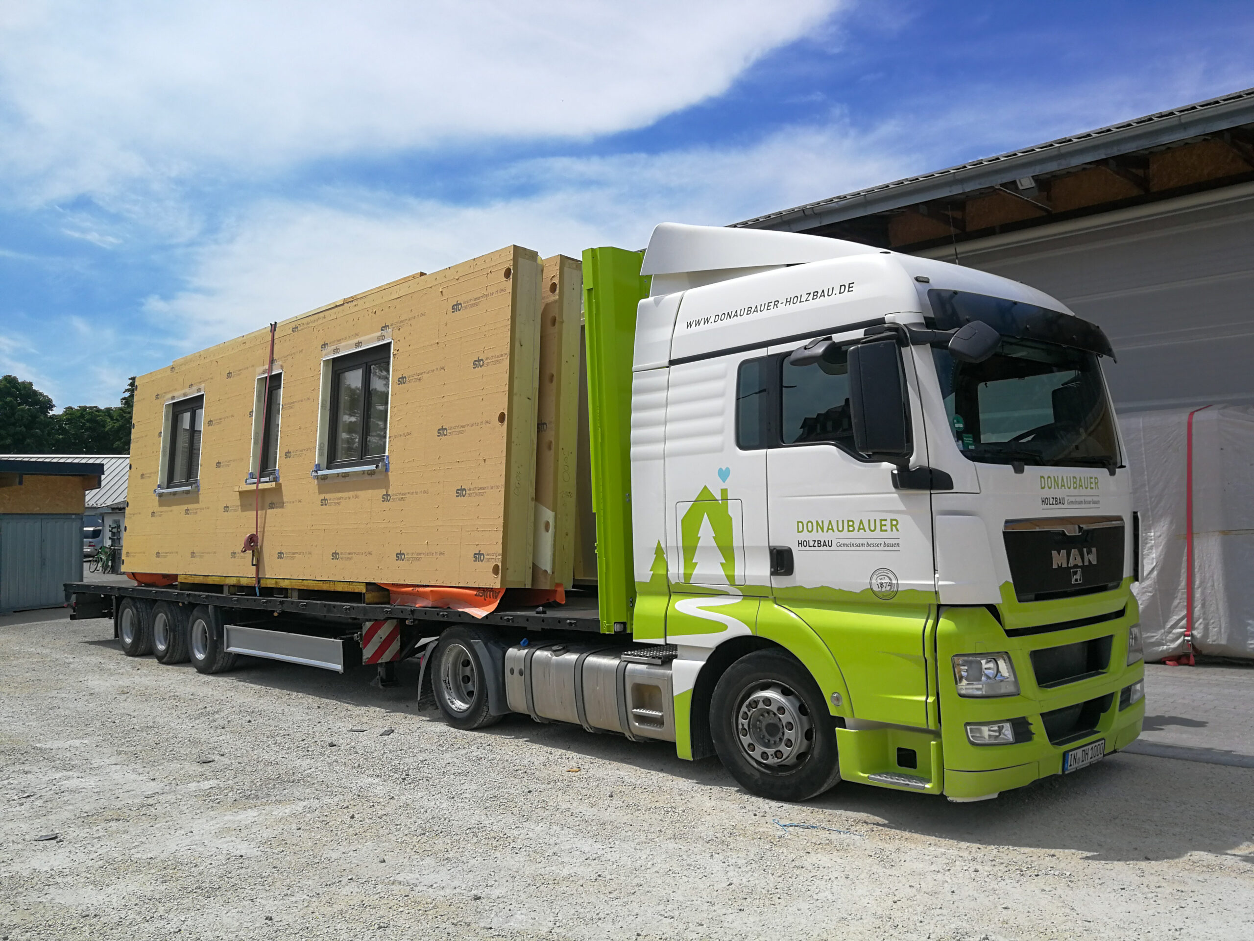 Lastwagen mit Donaubauer Holzbau Branding und aufgeladenen Wandelementen eines Holzhauses